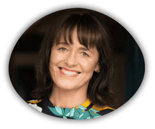 A woman with shoulder-length dark brown hair and fringe smiles warmly, wearing a floral-patterned top. The photo has a soft, oval-shaped border.