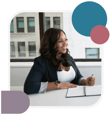 A woman in a navy blazer smiles as she writes in a notebook at a desk by a window, with teal, pink and purple shapes framing the photo.